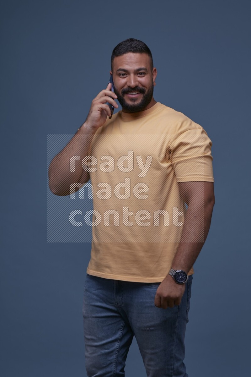 رجل يرتدي بنطال ازرق جينز وقميص اصفر بأكمام قصيره يتحدث بجواله