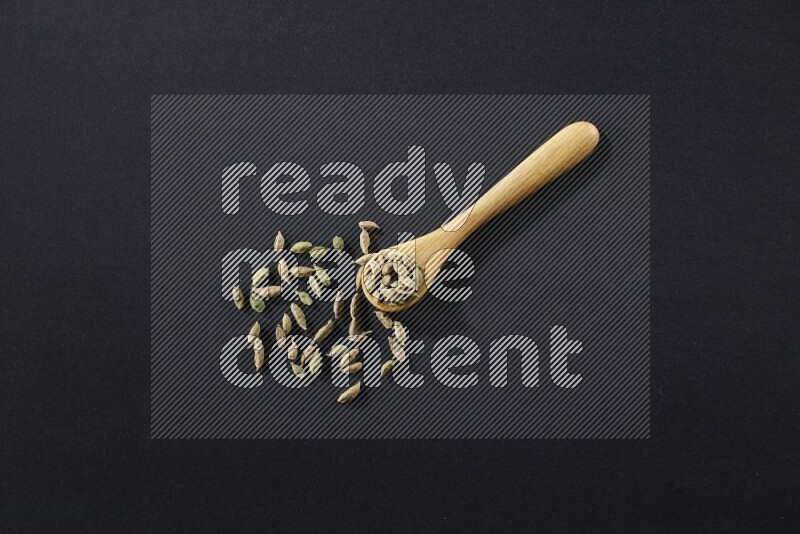 A wooden spoon full of cardamom on black flooring