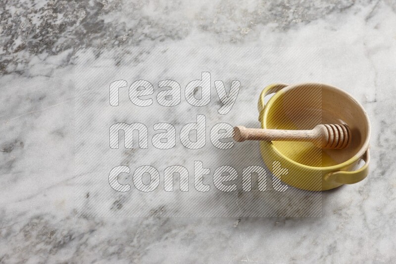 Multicolored pottery bowl with wooden honey dipper in it on grey marble background