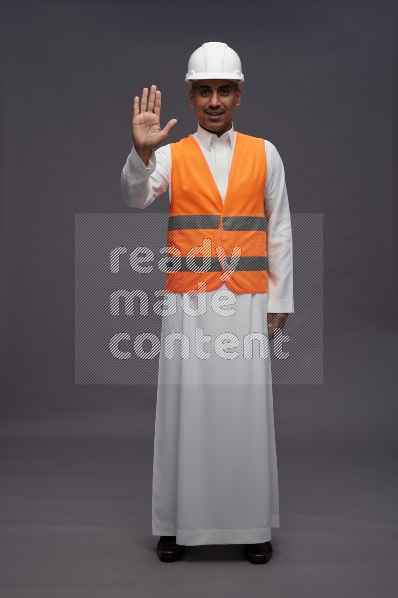 Saudi man wearing thob with engineer vest standing interacting with the camera on gray background