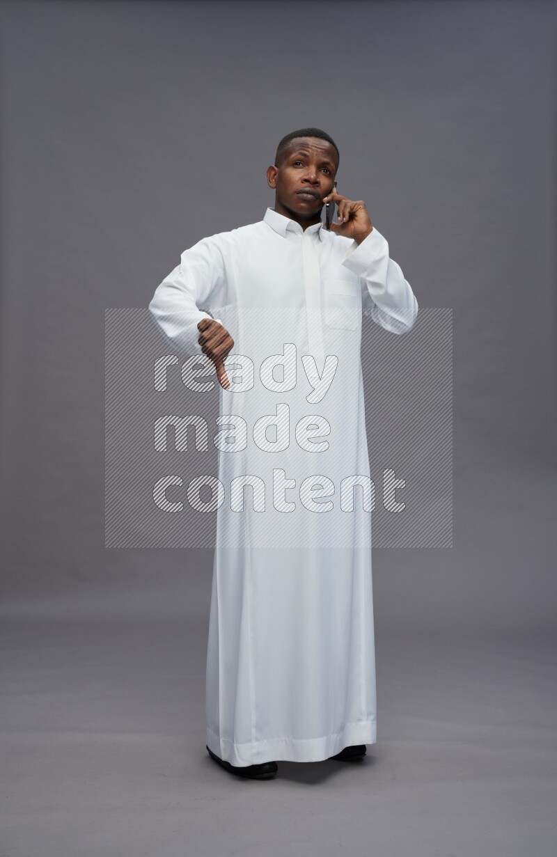 Saudi man wearing thob standing talking on phone on gray background