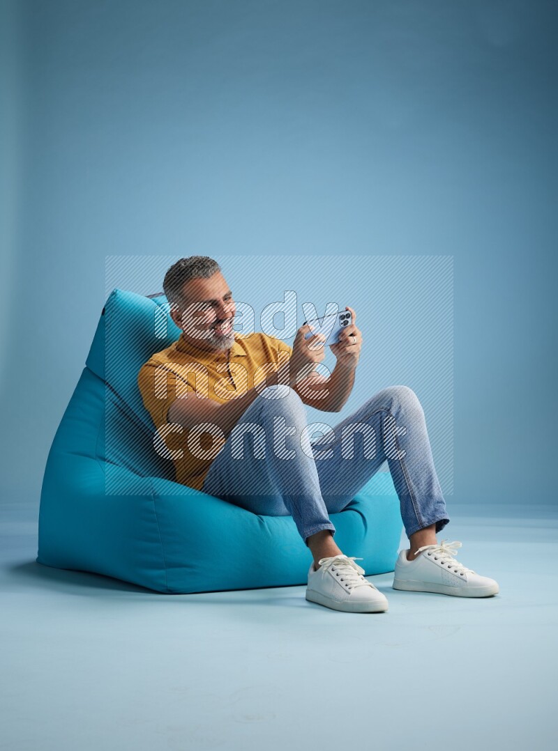 A man sitting on a blue beanbag and playing on phone