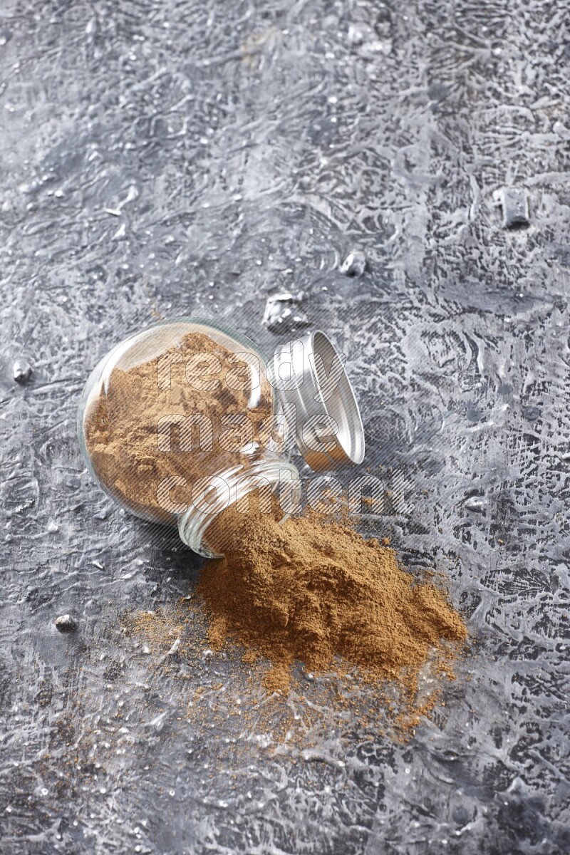 Flipped herbal glass jar full of cinnamon powder on textured black background