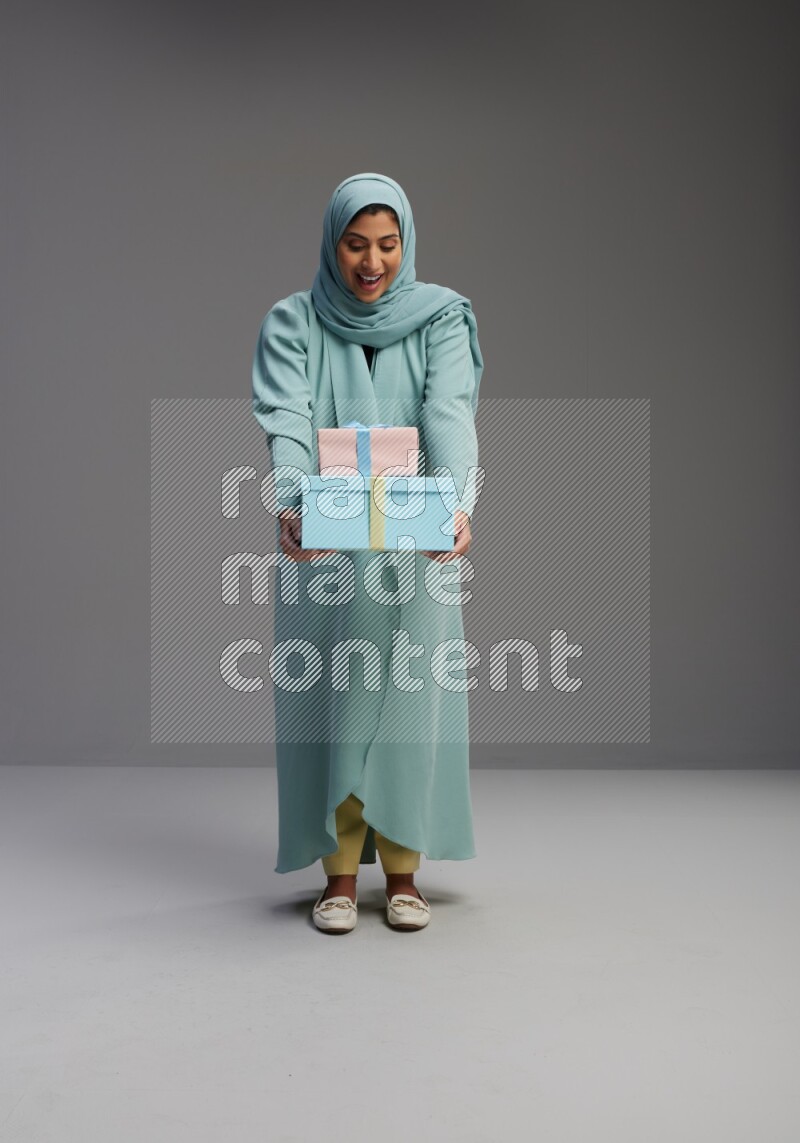 Saudi Woman wearing Abaya standing holding gift box on Gray background