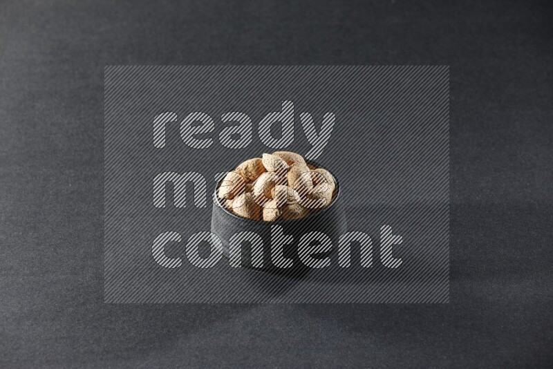 A black pottery bowl full of almonds on a black background in different angles