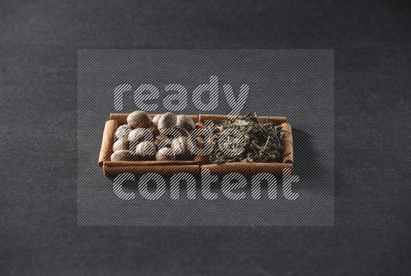 مربعان من أعواد القرفة ممتلئان بجوزة الطيب والريحان المجفف علي خلفية سوداء