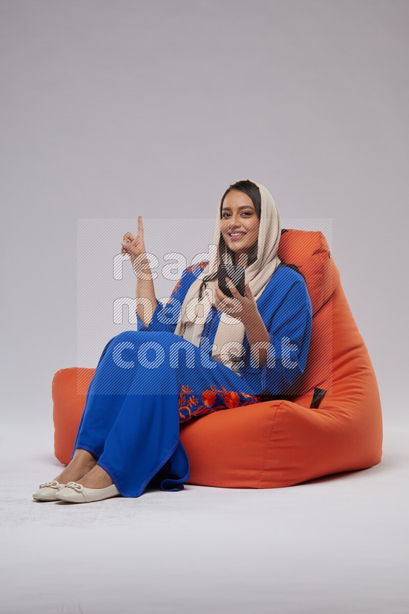 A Saudi woman sitting on an orange beanbag and texting on phone