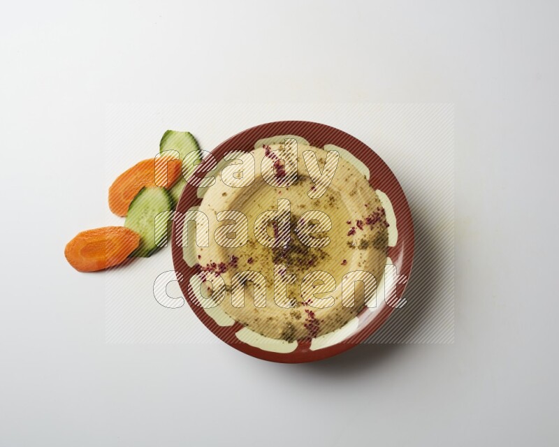 Hummus in a traditional plate garnished with zaatar & sumak on a white background