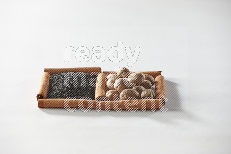 مربعان من أعواد القرفة ممتلئان بحبة البركة السوداء وجوزة الطيب علي خلفية بيضاء