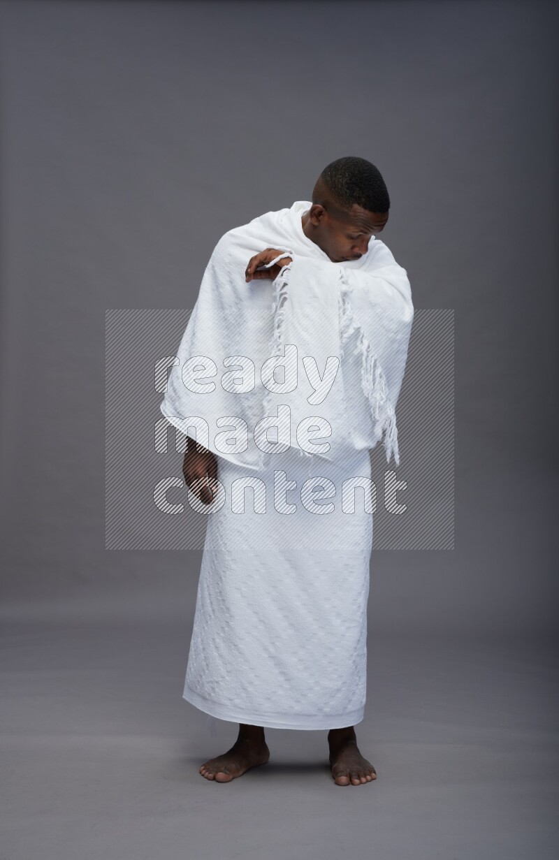 A man wearing Ehram standing showing how to sneeze on gray background
