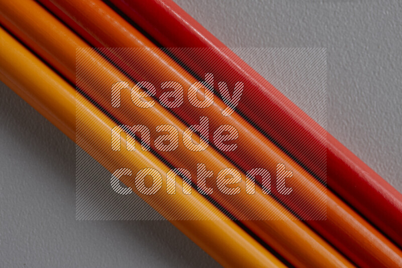 A collection of colored pencils arranged showcasing a gradient of orange hues on grey background