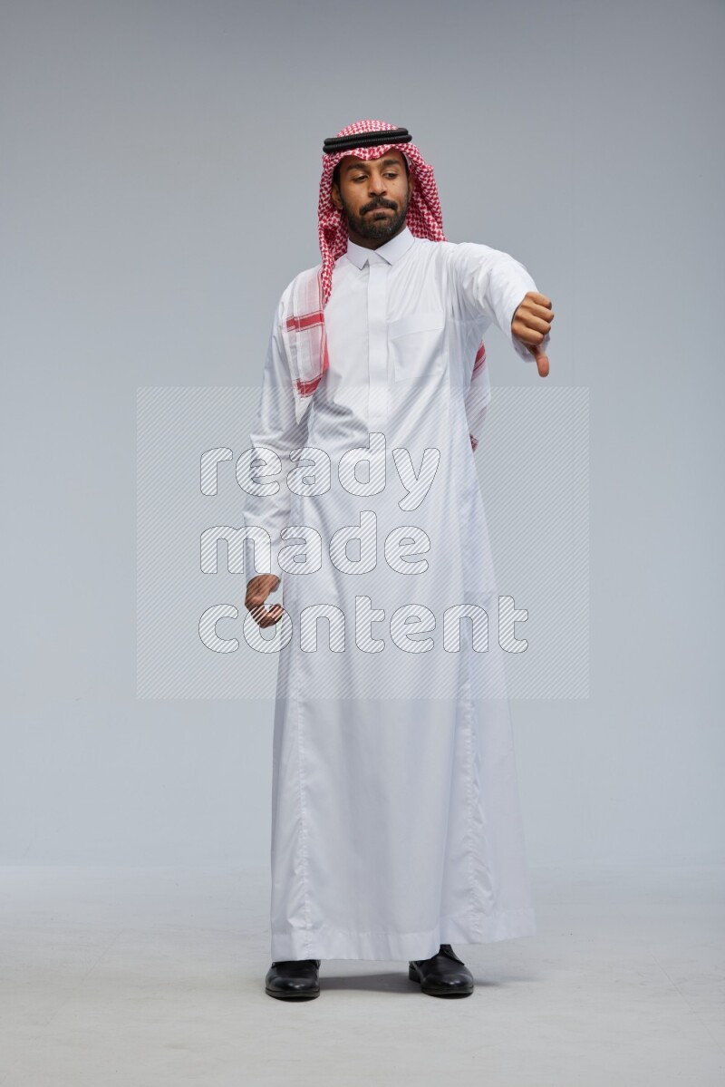 Saudi man Wearing Thob and shomag standing interacting with the camera on Gray background