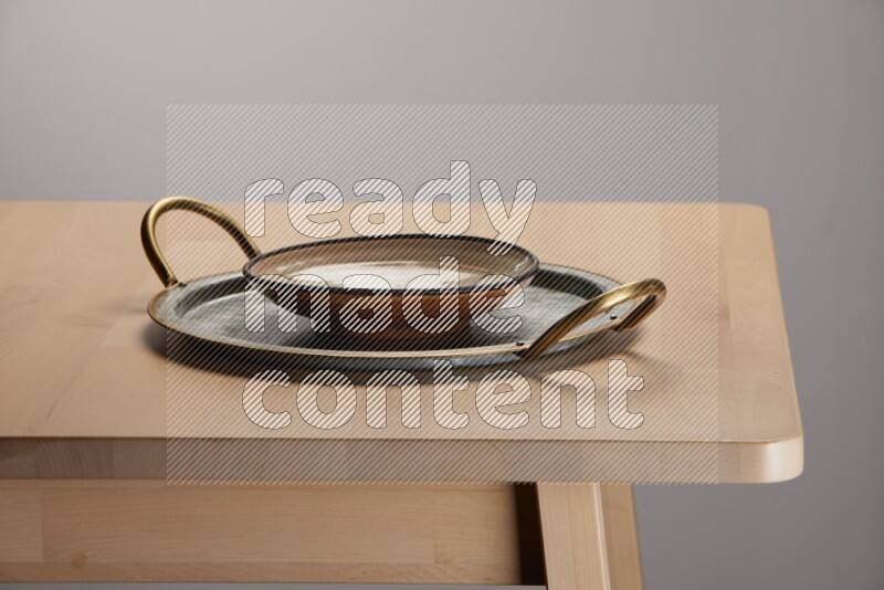 multicolored plate placed on a rounded stainless steel tray with golden handels on the edge of wooden table