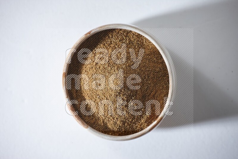 A beige bowl full of cumin powder on a white flooring