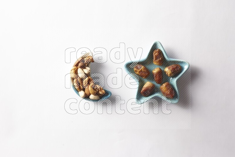 Dates in a star shaped pottery plate and a crescent plate with mixed nuts on white background