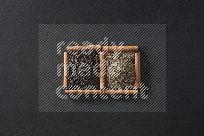 مربعان من أعواد القرفة ممتلئان بحبوب الفلفل الأسود وحبوب الكمون علي خلفية سوداء