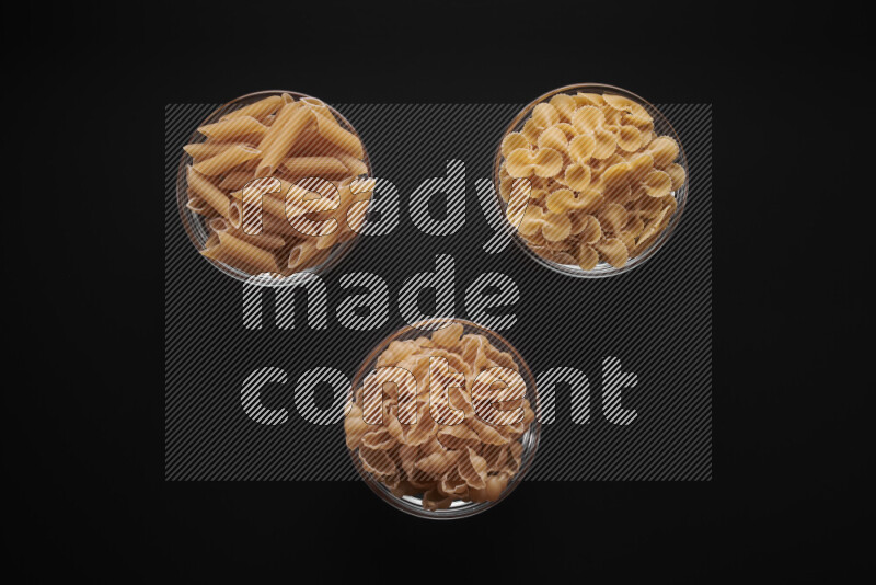 Different pasta types in glass bowls on black background