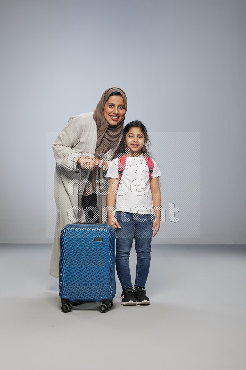 Mom and daughter standing pulling a carry-on bag on gray background