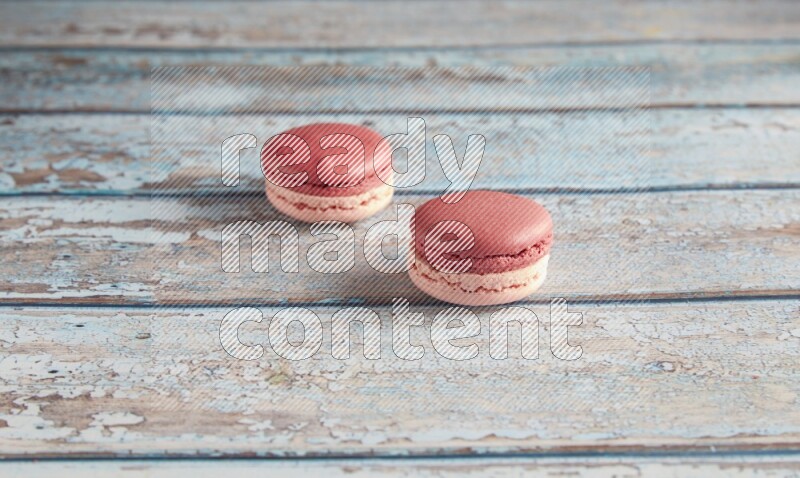 45º Shot of two Pink Litchi Raspberry macarons on light blue wooden background