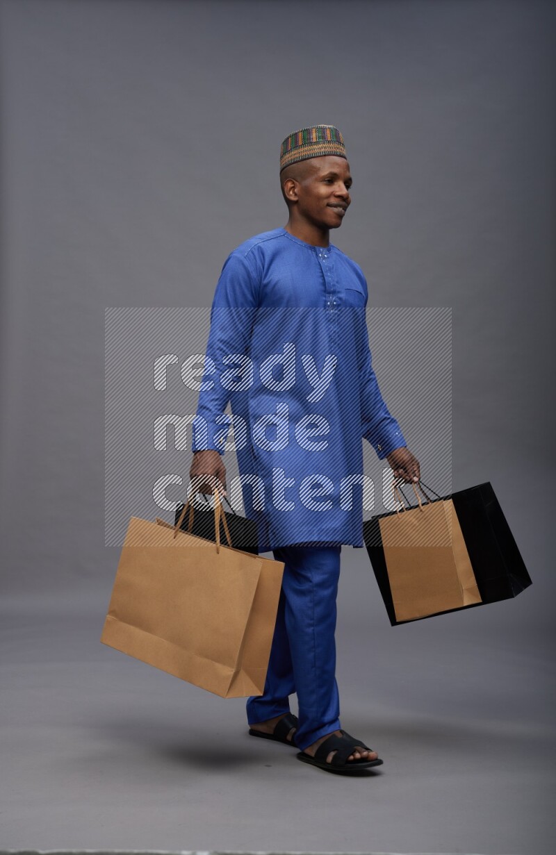 Man wearing Nigerian outfit standing holding shopping bag on gray background