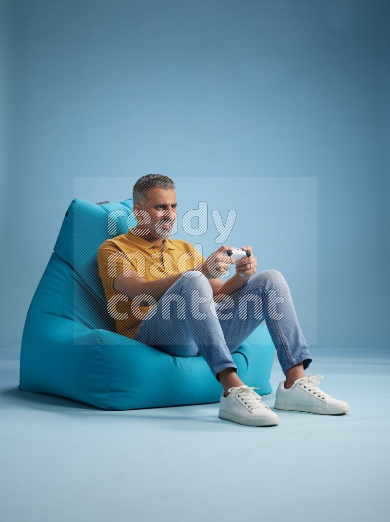 A man sitting on a blue beanbag and gaming with joystick