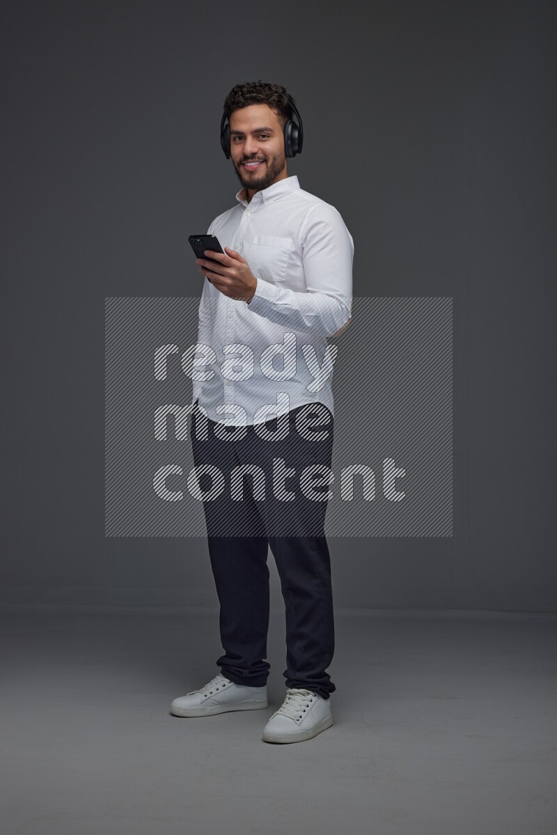 A man wearing smart casual and using his phone and headphone eye level on a gray background