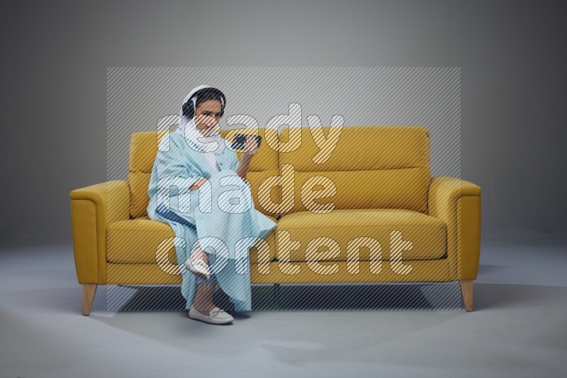A Saudi woman sitting on a yellow Sofa Watching a Movie wearing Blue Abaya