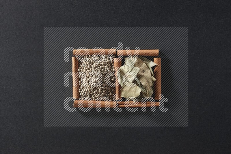 2 squares of cinnamon sticks full of white peppers and bay laurel leaves on black flooring