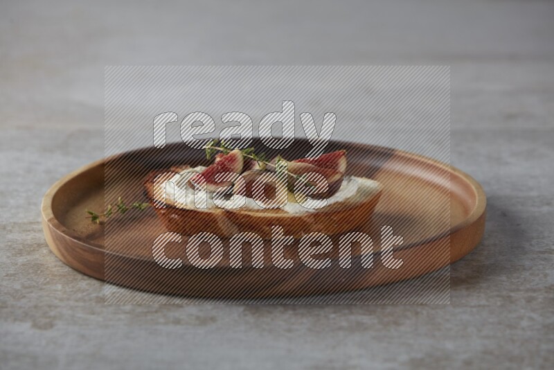 quarters of figs with cream cheese on toasted sourdough slice on a wooden board on textured grey background