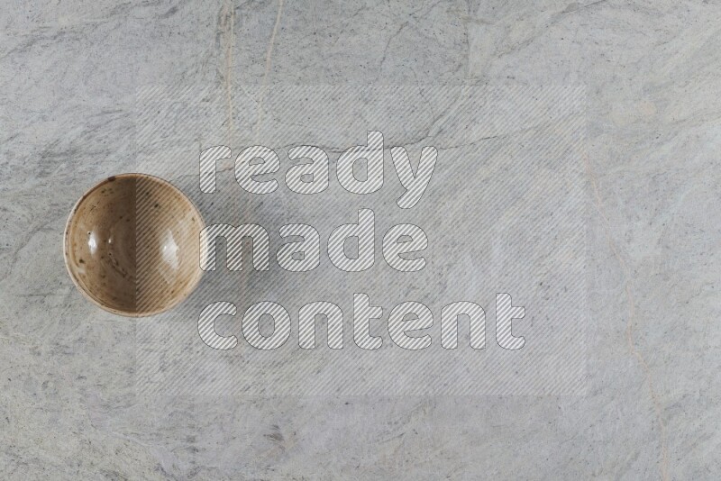 A small beige pottery bowl on grey marble background