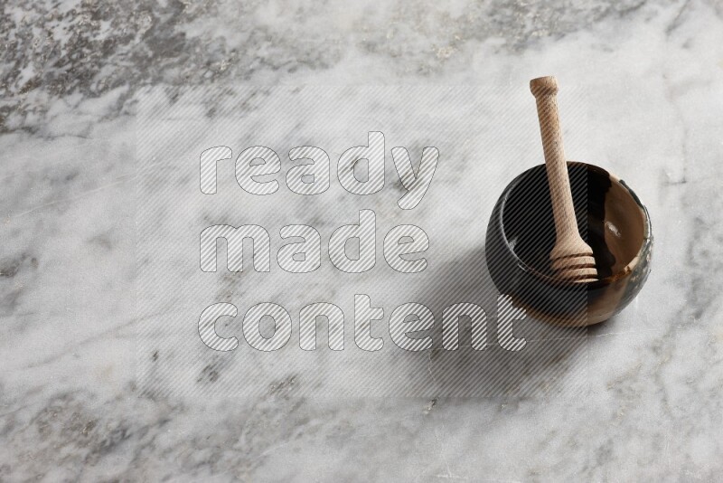 Multicolored pottery bowl with wooden honey dipper in it on grey marble background