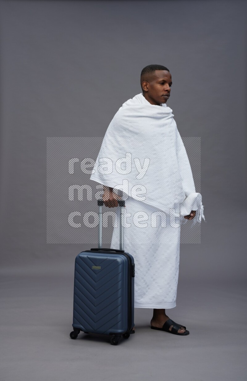 A man wearing Ehram Standing holding traveling bag on gray background