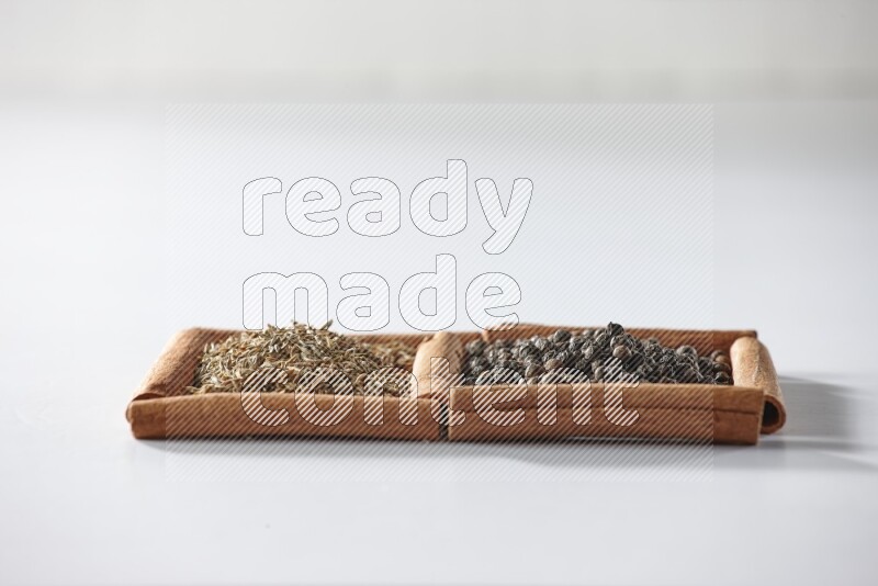 مربعان من أعواد القرفة ممتلئان بحبوب الفلفل الأسود وحبوب الكمون علي خلفية بيضاء