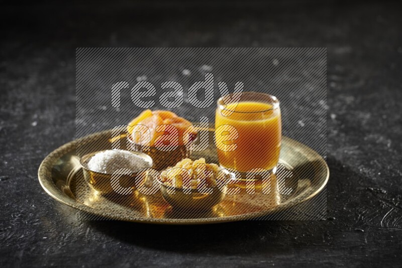 Dried fruits in metal bowls with qamar eldin on a tray in dark setup