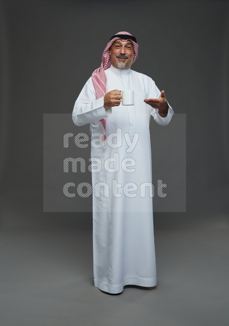 Saudi man with shomag Standing holding mug on gray background