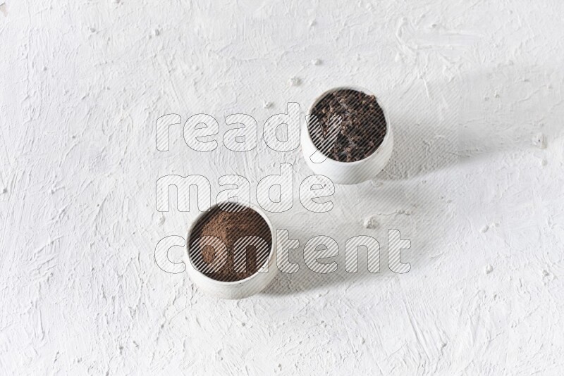 2 Beige ceramic bowls, one full of cloves and the other full of powder on textured white flooring