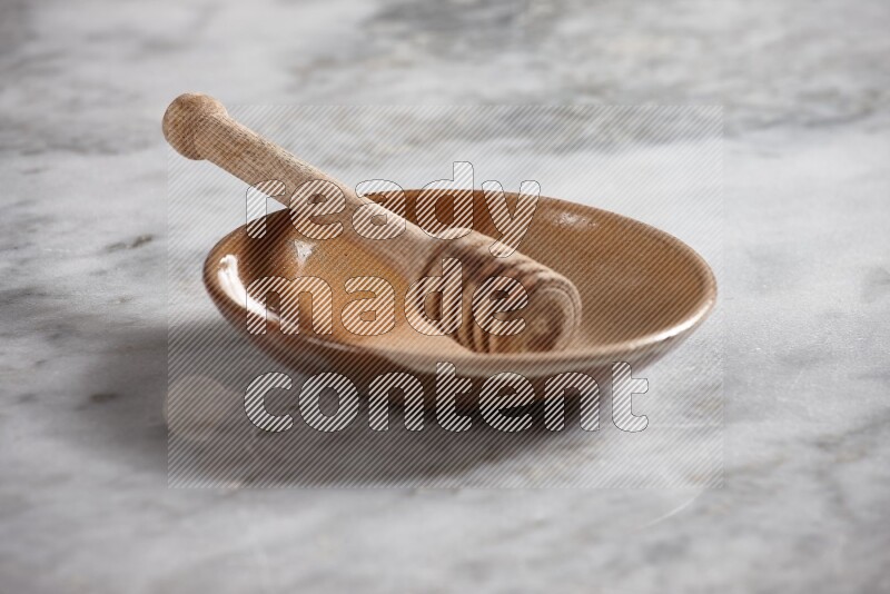 Multicolored pottery plate with wooden honey dipper in it on grey marble background