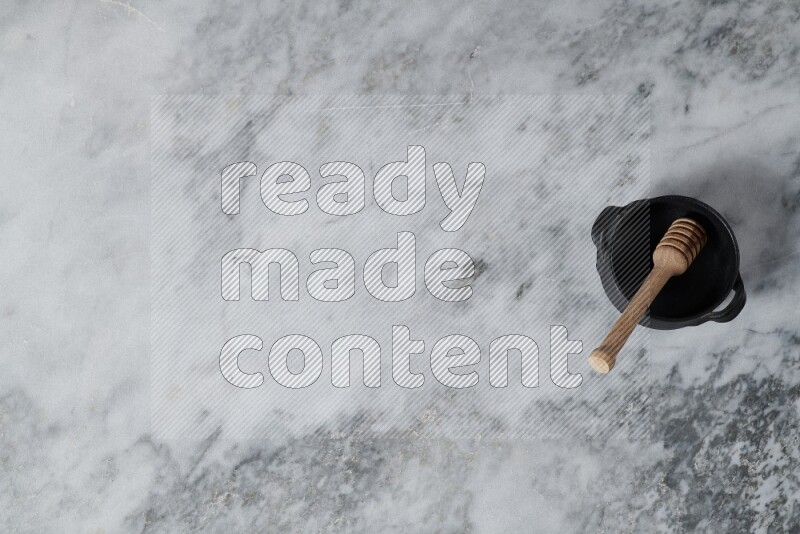 Black pottery bowl with wooden honey dipper in it on grey marble background
