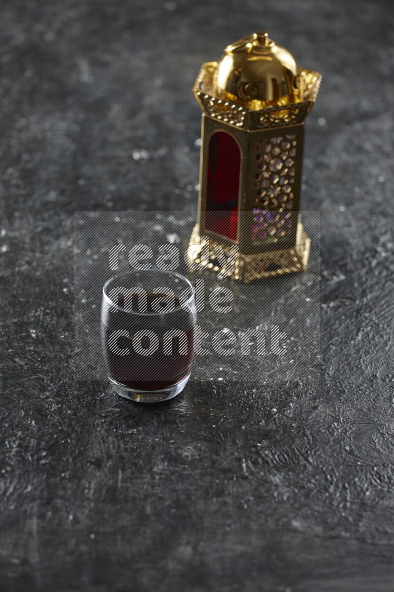 A golden lantern with different drinks, dates, nuts, prayer beads and quran on textured black background