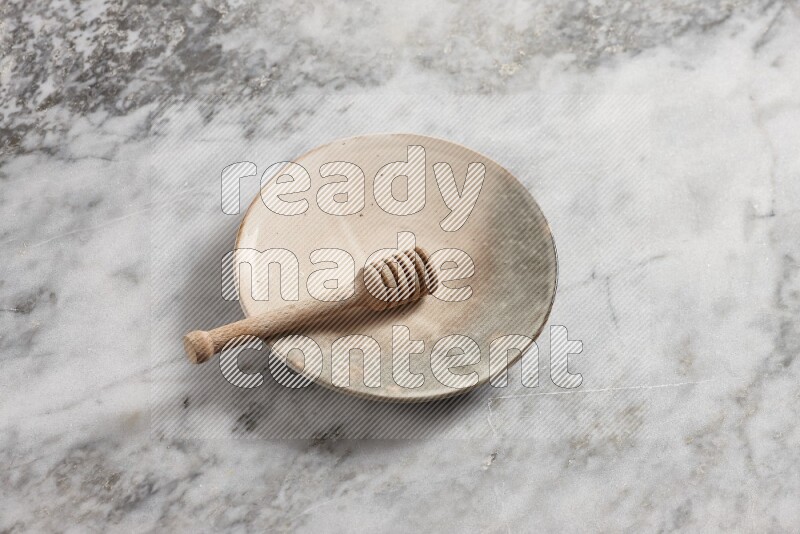 Multicolored pottery plate with wooden honey dipper in it on grey marble background