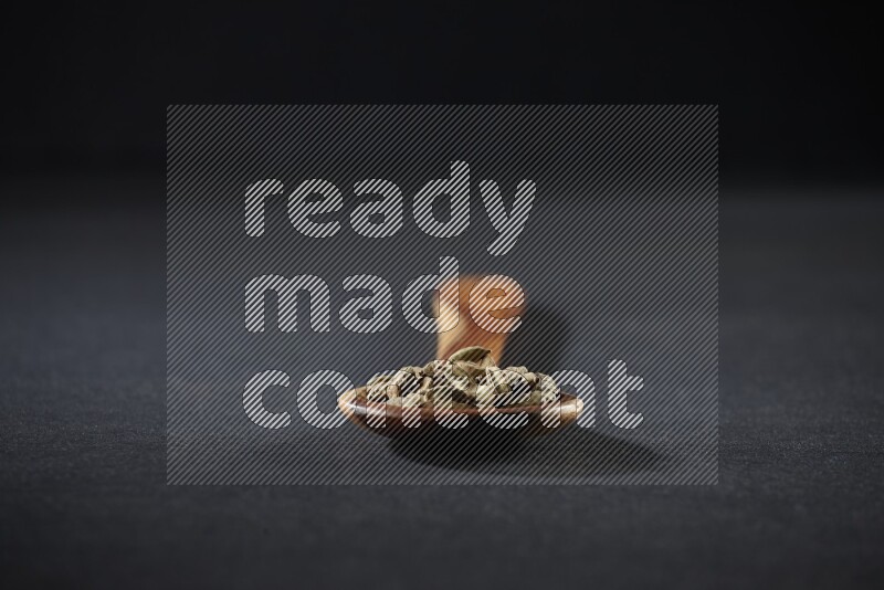 A wooden ladle full of cardamom on black flooring