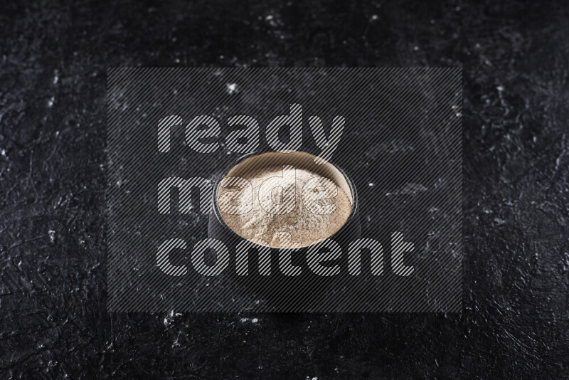 A black pottery bowl full of onion powder on black background