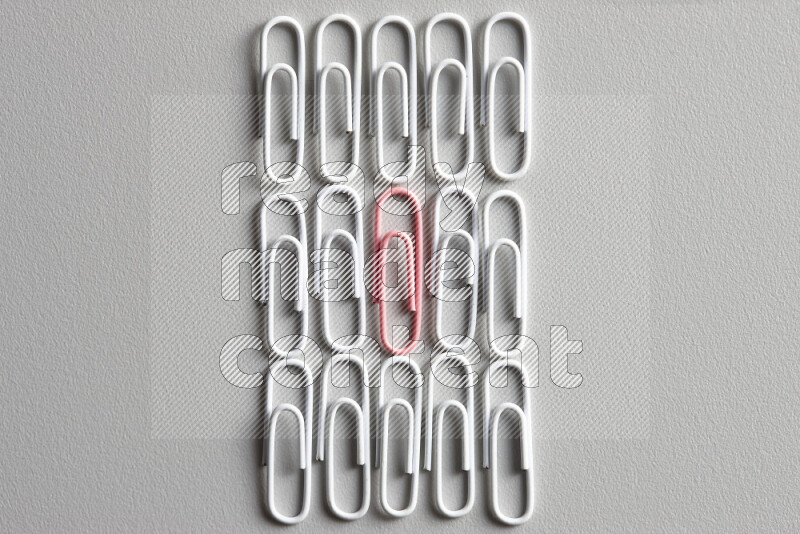A bunch of white paper clips with a different colored paper clip in the center on grey background