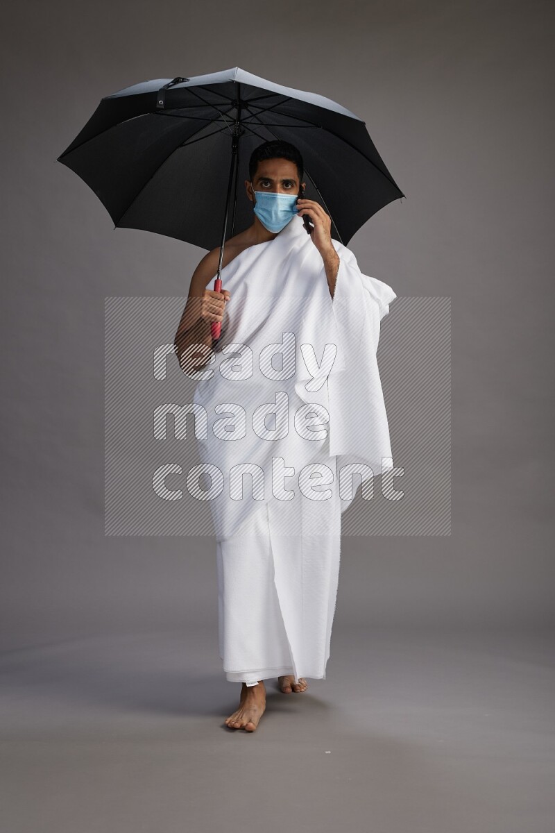 A man wearing Ehram and mask Standing holding umbrella on gray background on gray background