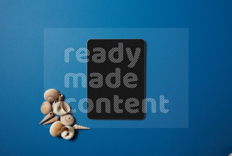 top view shot of a tablet, and seashells on blue background