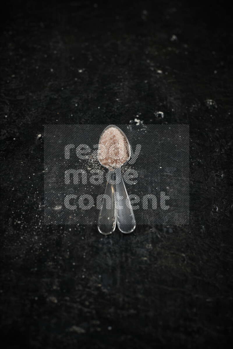 2 metal spoons filled with pink himalayan salt on black background