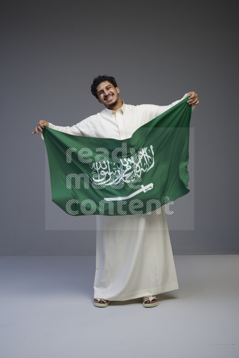 رجل سعودي يرتدي ثوب ابيض ويحمل العلم السعودي