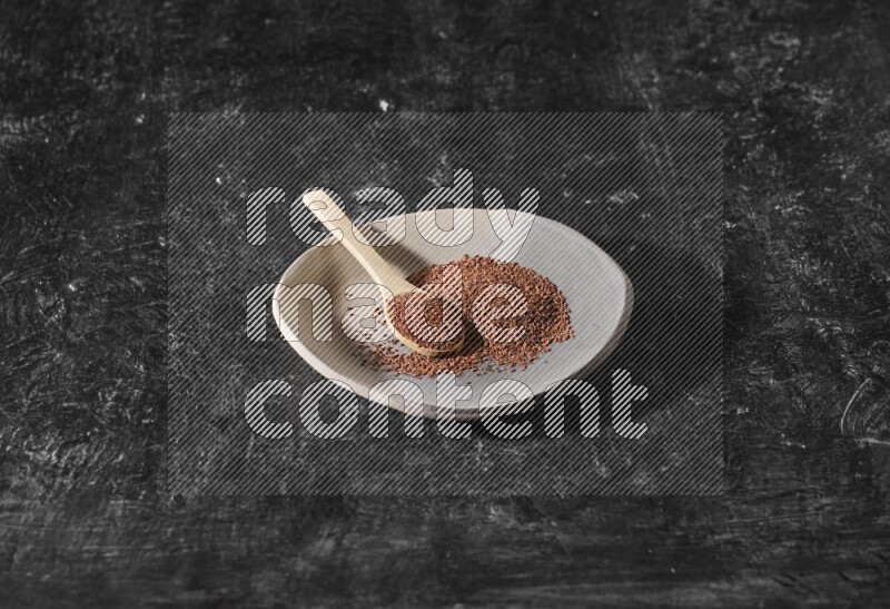 A multicolored pottery plate full of garden cress seeds and wooden spoon full of seeds on a textured black flooring