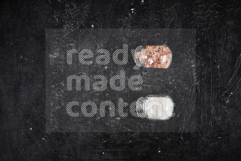 2 وعاء زجاجي احدهمها ممتلئ بملح الهيمالايا الخشن والأخر بملح البحر الخشن على خلفية سوداء