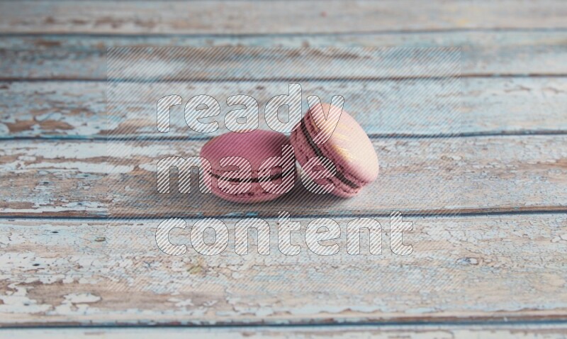 45º Shot of two Purple Strawberry macarons on light blue wooden background